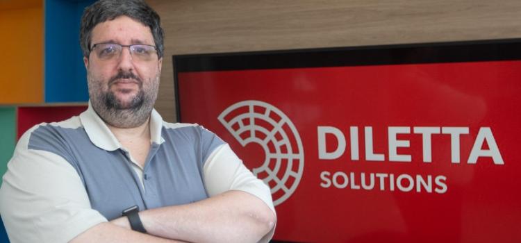 Michel Cusnir é um homem branco com barba e cabelos grisalhos, veste camisa polo bicolor e usa óculos metálico. Ao fundo uma tela exibe o logotipo da Diletta em cores branca e vermelha. Fim da descrição.