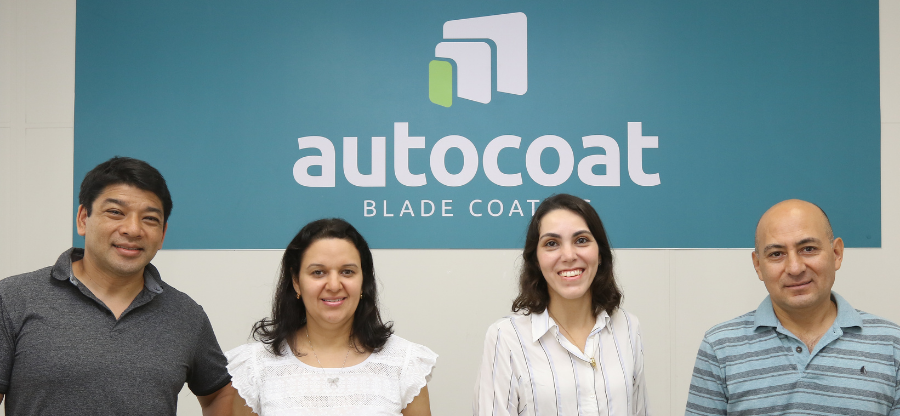 Na fotografia estão quatro pessoas que fazem parte do time da startup AutoCoat. Eles estão a frente de uma parede que está pintada de azul e branco e contém o logo da empresa. O time conta com dois homens e duas mulheres. Fim da descrição.