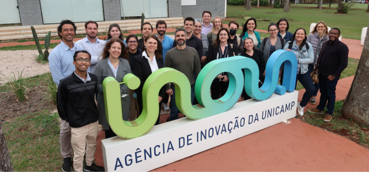 Grupo de pessoas em torno do logo da Inova Unicamp na frente da sede da Agência. 