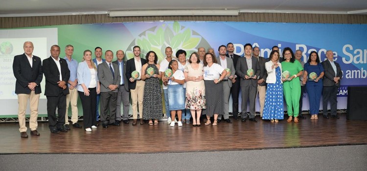 Foto colorida dos premiados e autoridades no palco do hotel Nacional Inn em Campinas. Fim da descrição.