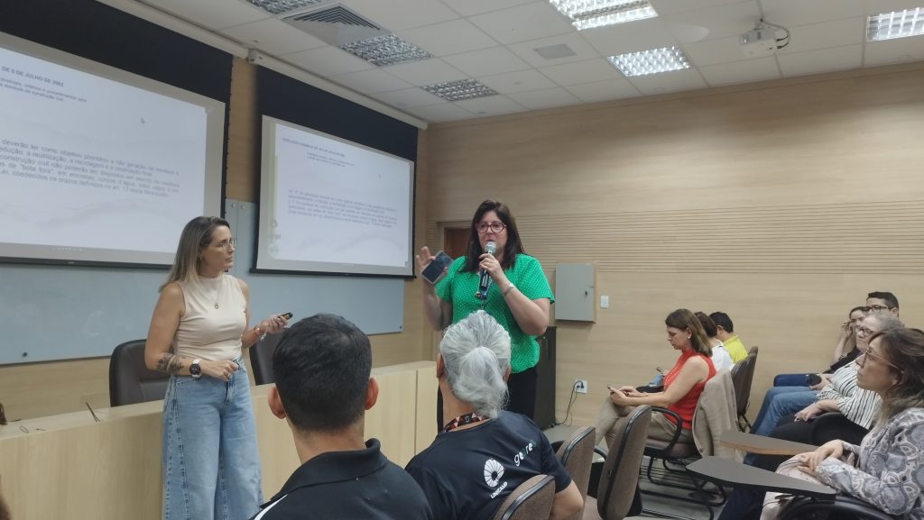 Em pé, à esquerda está Amanda Roberta de Almeida, com camisa clara. À direita está a professora Carmenlucia Giordano, de camisa verde. Fim da descrição.