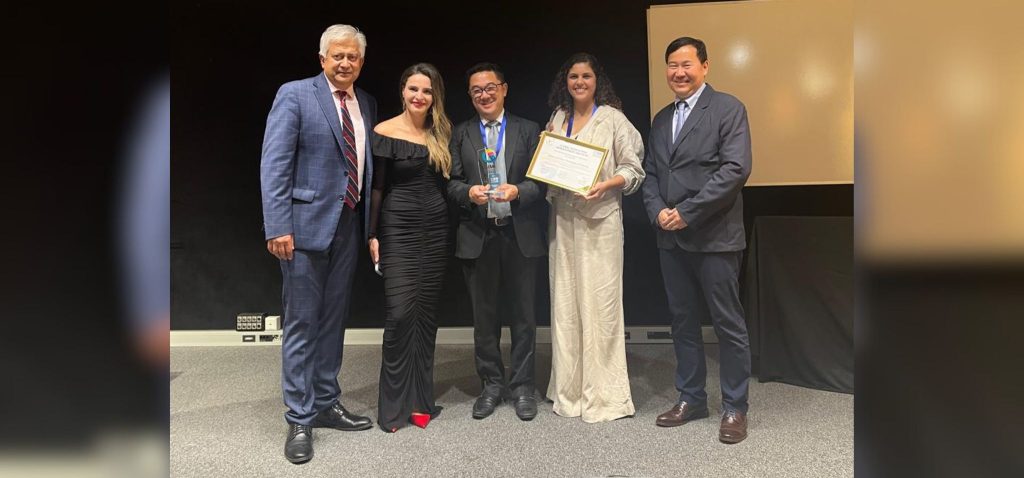 Foto posada de cinco pessoas, entre elas, dois representantes do Parque Científico e Tecnológico da Unicamp. Um deles, uma mulher, carrega o certificado que garante ao Parque a premiação obtida no GIMI Innovation Awards. Eles estão em pé, lado a lado, sorrindo para a foto. Fim da descrição.