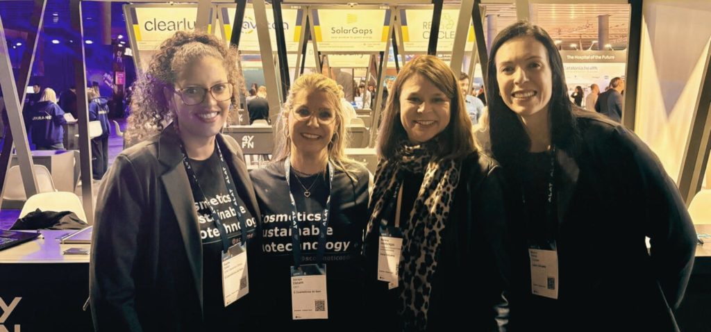 Foto de quatro mulheres sorrindo para a câmera em frente a estandes do evento em Barcelona, o 4 Years From Now. Fim da descrição.